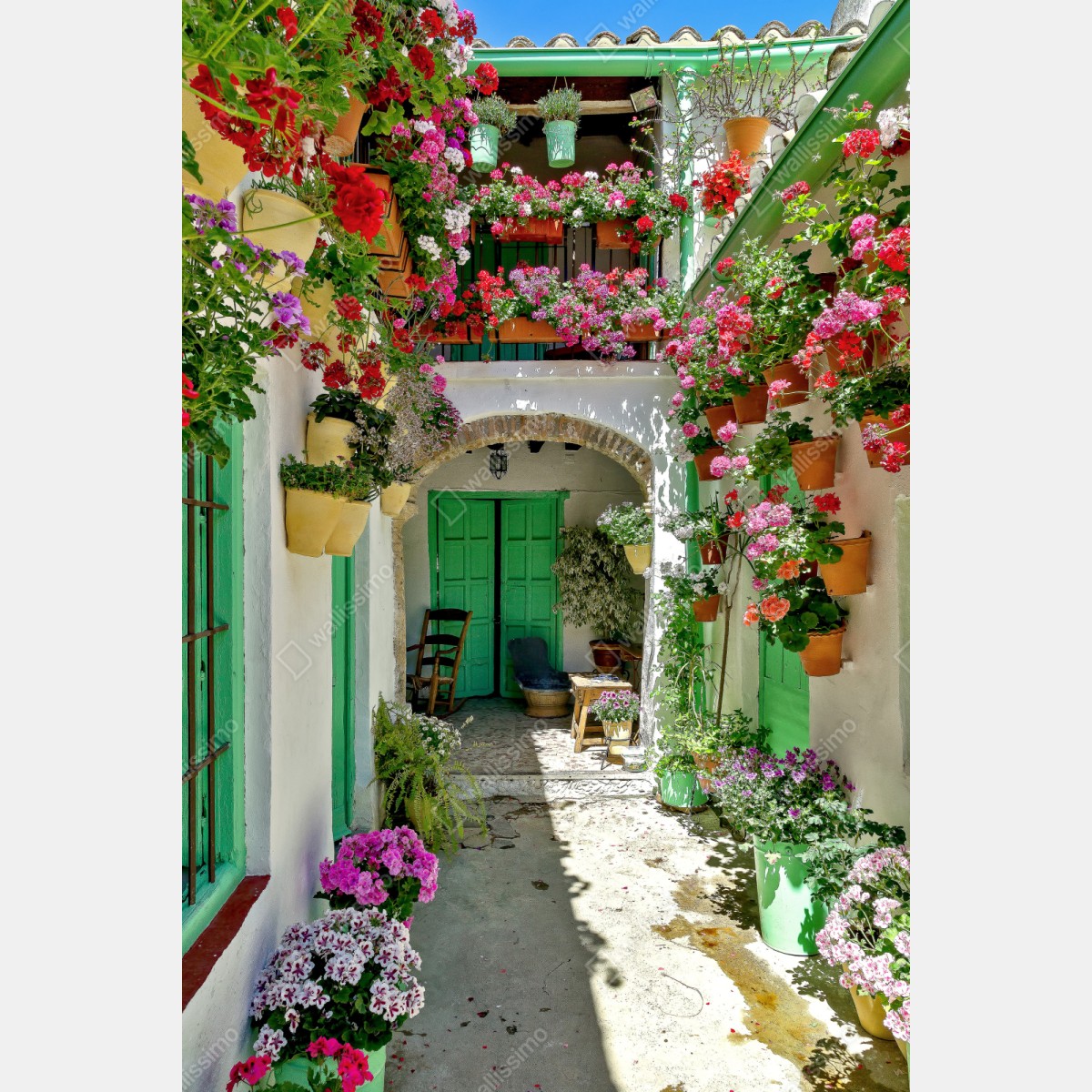 Naklejka repozycjonowalna słoneczne podwórko pełne kwiatów i zielonych drzwi – Wallissimo® Naklejka repozycjonowalna słoneczne podwórko pełne kwiatów i zielonych drzwi – Wallissimo®